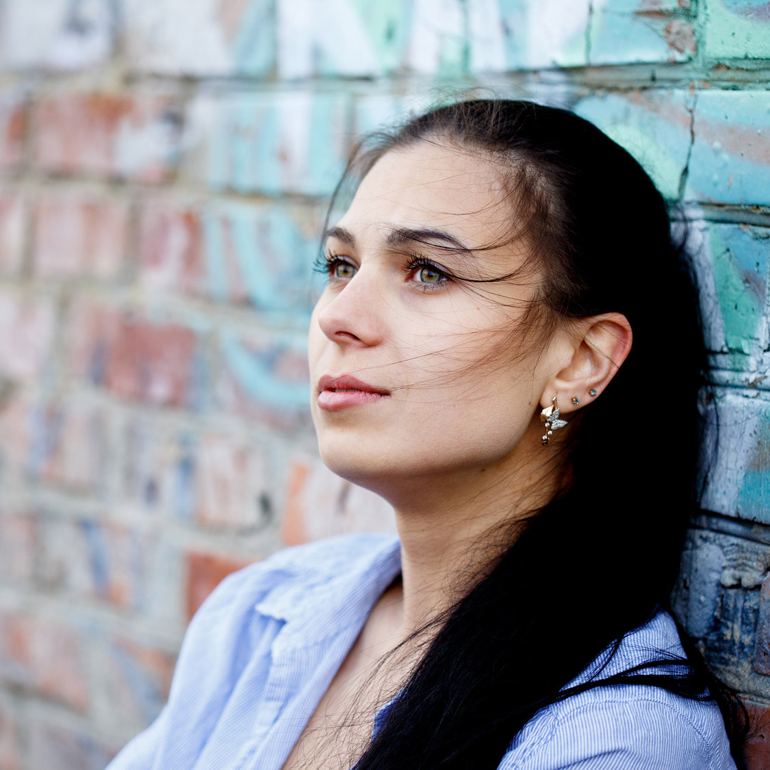A woman sits against a brick wall and stares into space